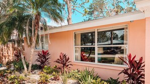 A house with a large window, surrounded by a garden with various plants and a palm tree. - The Coral Cottage close to all that Sarasota has to offer (Sarasota)