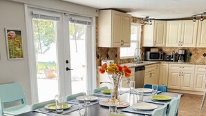 A dining area with a table set for four, surrounded by teal chairs, in a room with wooden flooring and light-colored walls. - The Coral Cottage close to all that Sarasota has to offer (Sarasota)