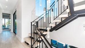 A modern staircase with black railings and wooden steps, leading to a second floor. - Premier Coastal Elegance in Corona Del Mar | Expansive Rooftop Deck | Luxury Interior (Corona Del Mar)