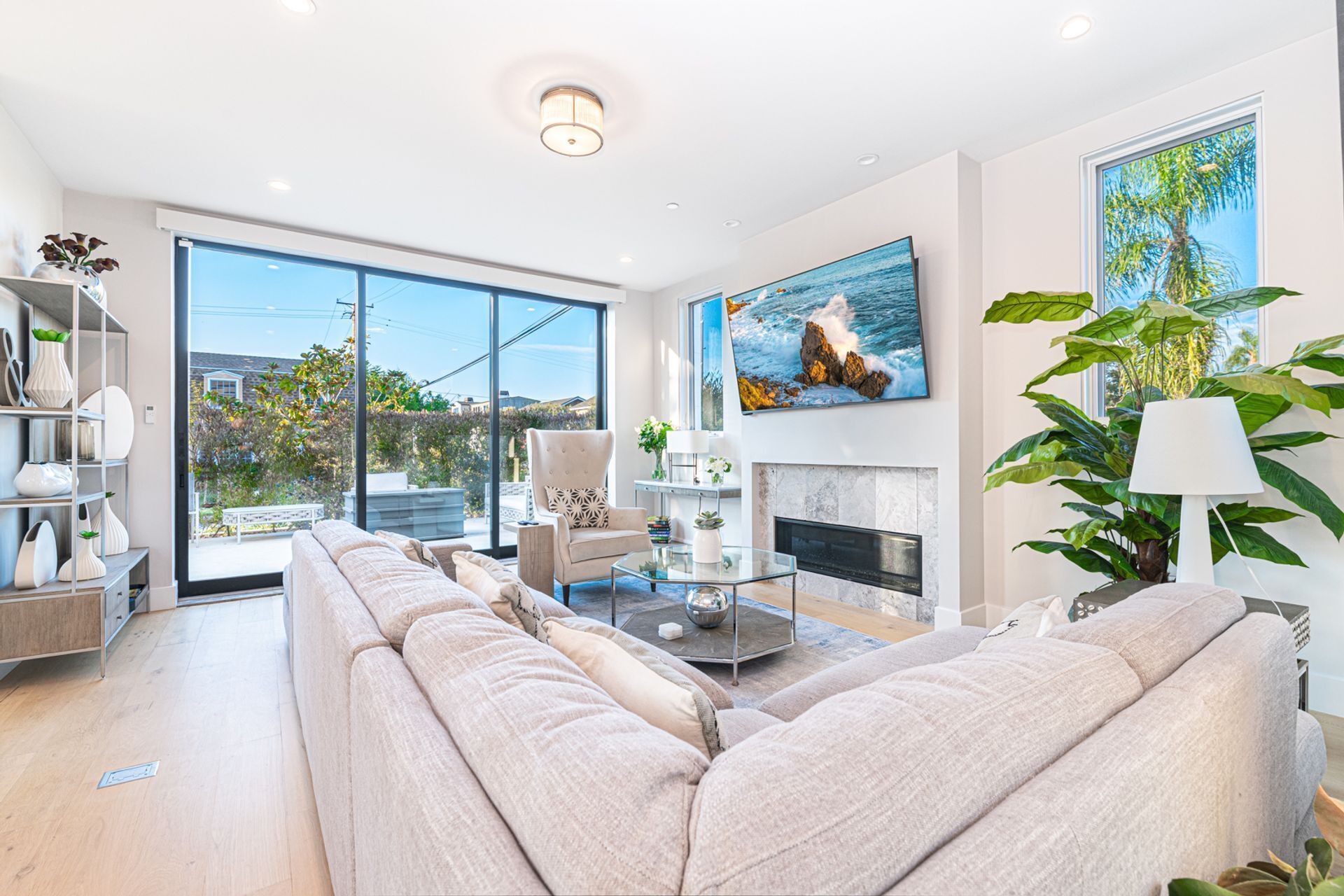 A spacious living room with a large sofa, a fireplace, and a large window overlooking a garden.