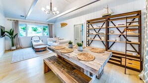 A spacious living room with a large wooden dining table, a white sofa, and a wooden bookshelf. - Oasis heaven close to everything you need! (East Hampton)