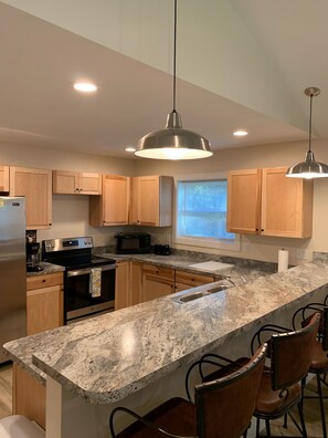 A modern kitchen with granite countertops, stainless steel appliances, wooden cabinets, and pendant lighting.