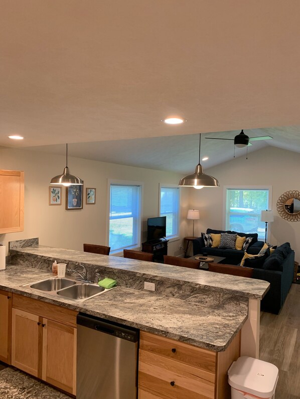 A modern kitchen with granite countertops, stainless steel appliances, and wooden cabinets. There is a dining area with a dark-colored sofa and a coffee table.