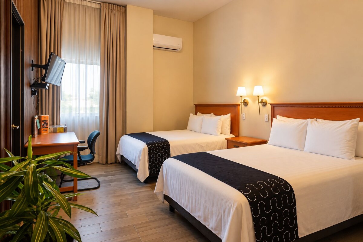 A hotel room with two beds, a desk with a chair, a TV, and a plant.