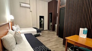 Una habitación de hotel con dos camas, una mesa de madera, un cubo de basura y una araña.