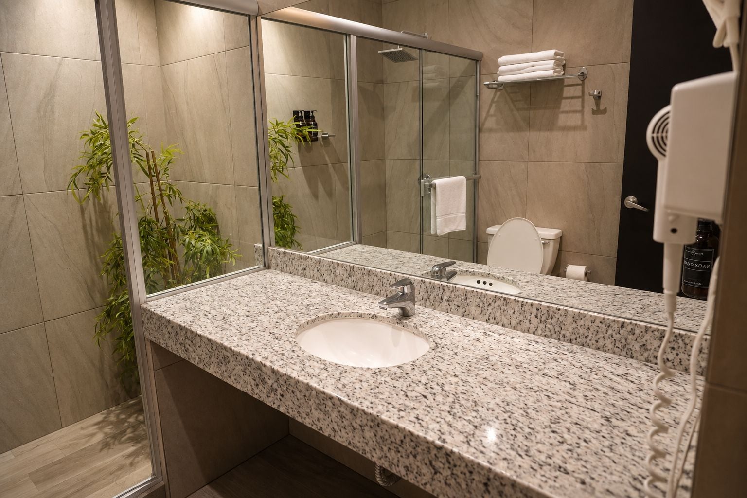 A modern bathroom with a granite countertop sink, a glass shower enclosure, and a large mirror.