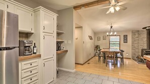 Una cocina moderna con armarios blancos, un refrigerador de acero inoxidable y un comedor con mesa y sillas de madera.