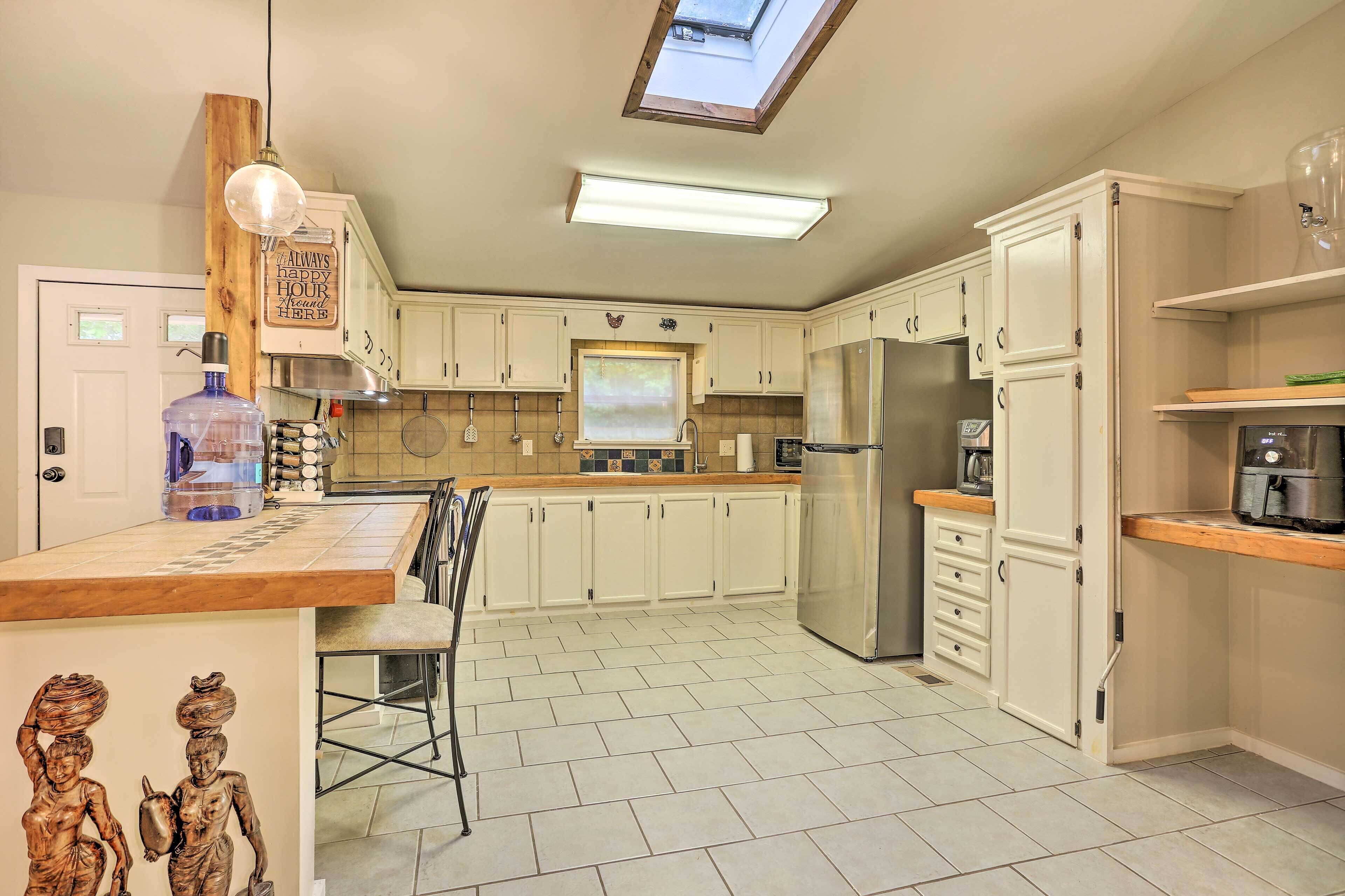 A kitchen with white cabinets, a stainless steel refrigerator, a large water dispenser, and a skylight above the countertop.