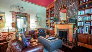 Een gezellige woonkamer met een leren bank, een gestreept voetenbankje, een open haard en een boekenkast vol boeken.