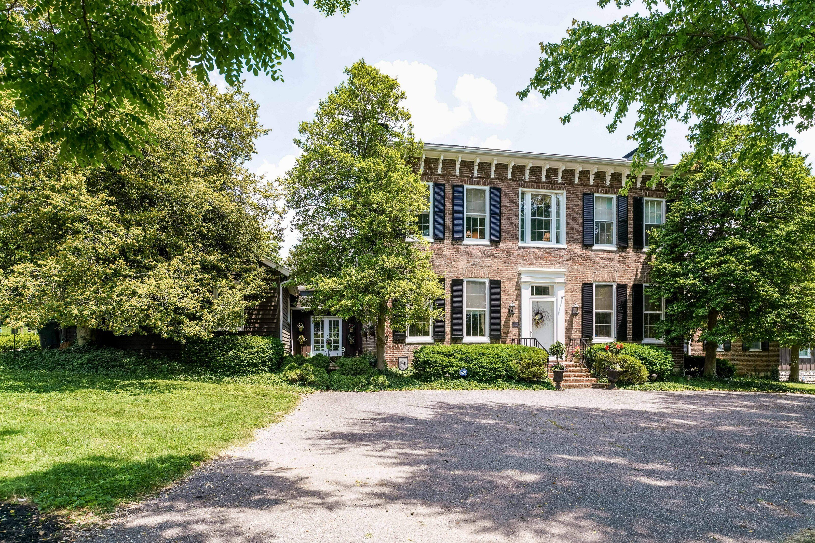 A two-story brick building with a front entrance, a driveway, and surrounding greenery.
