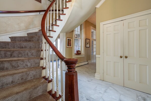 A grand staircase with a wooden handrail and carpeted steps leading to a white door. - Cheerful 8-Bedroom, 6-Bath Historic Mansion in Derby City – Ideal Vacation Home! (Louisville)