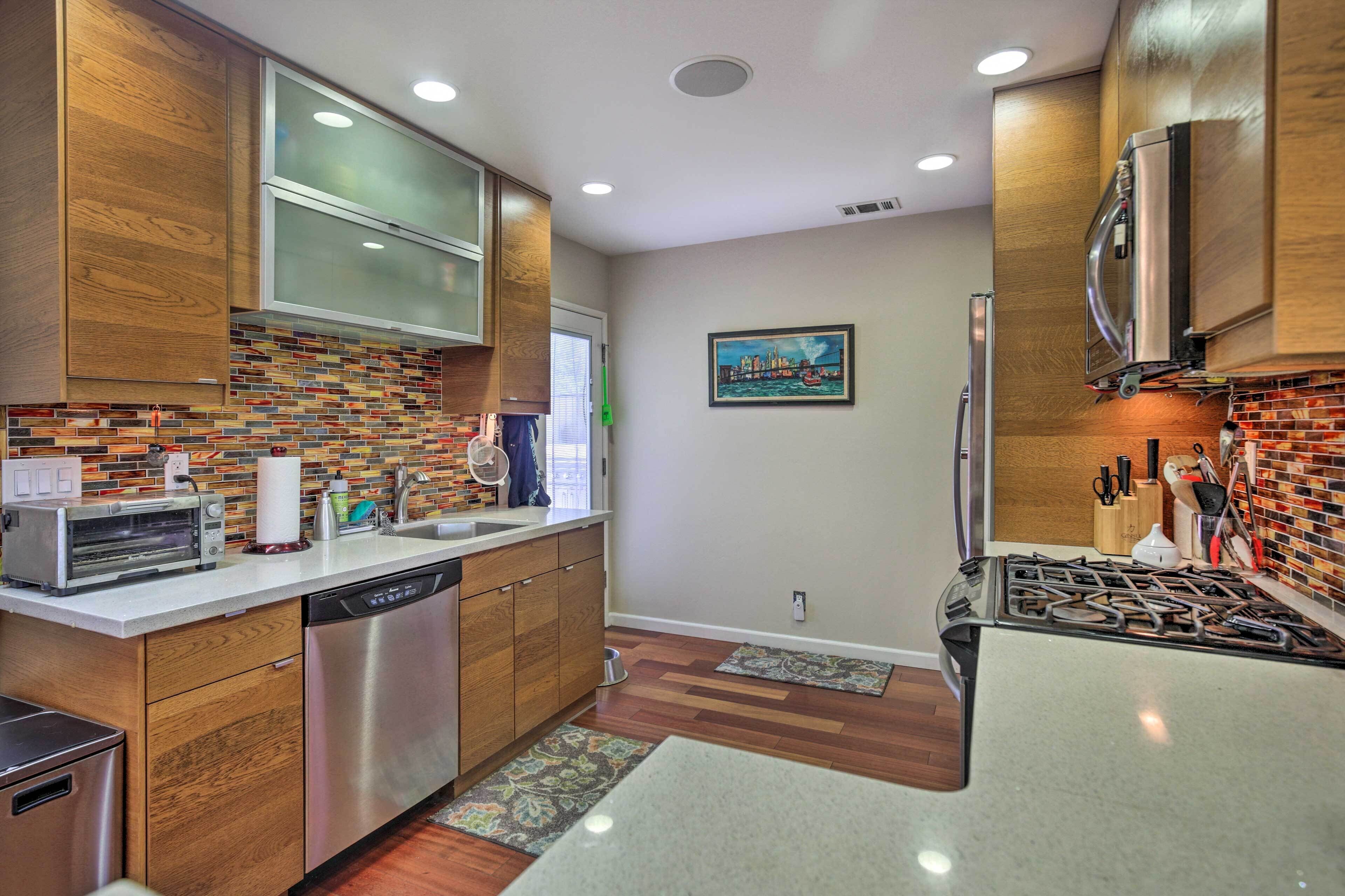 A modern kitchen with wooden cabinets, a dishwasher, a stove, and a window with a cityscape view.