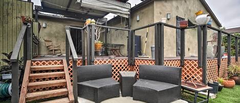 Un patio con mobiliario exterior, una escalera de madera y una zona de estar cubierta.
