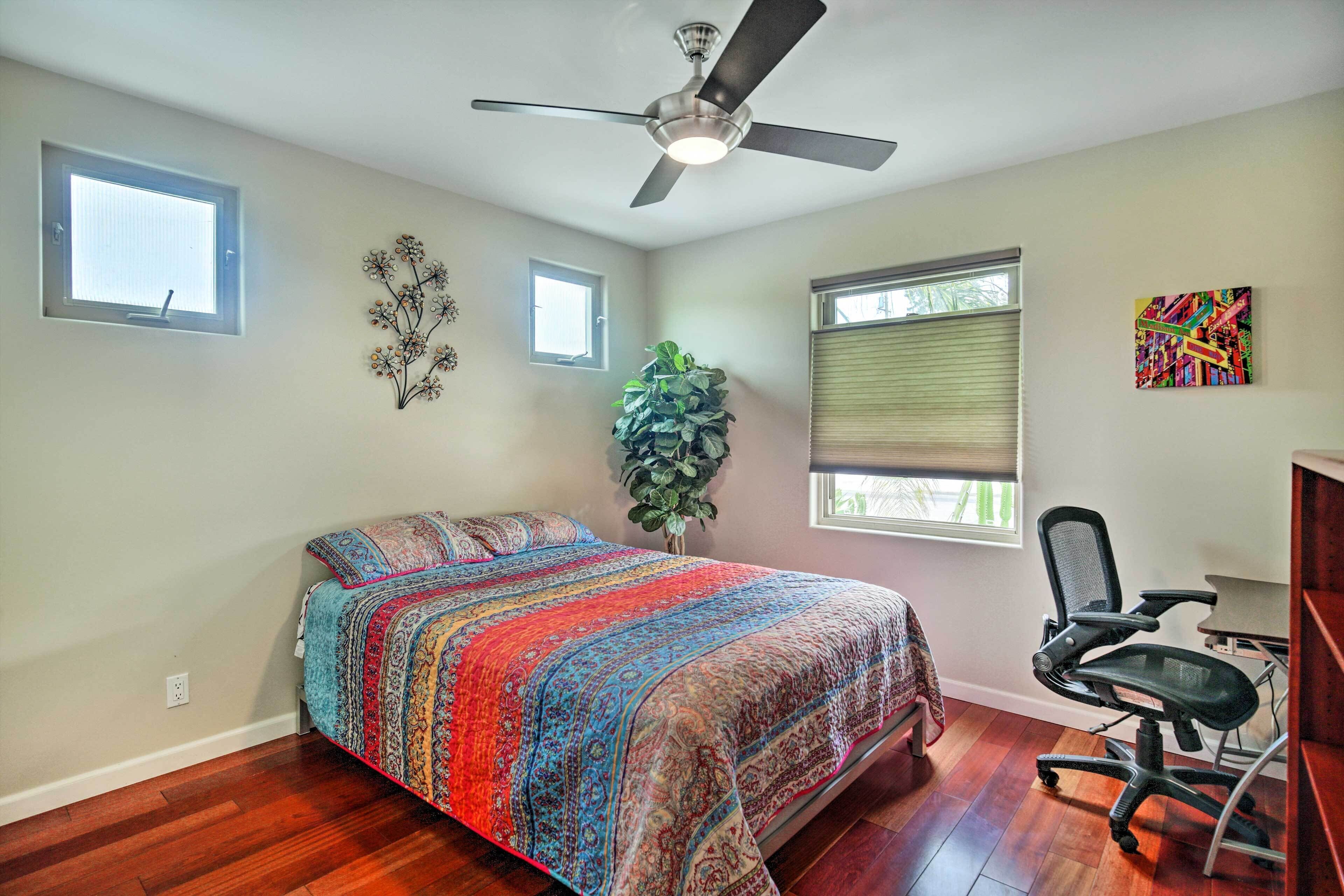 A bedroom with a bed, a desk, a chair, a ceiling fan, and a window.