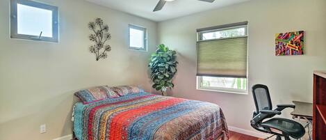A bedroom with a bed, a desk, a chair, a ceiling fan, and a window.