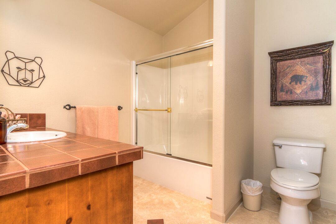 A bathroom with a wooden vanity, a glass shower enclosure, a toilet, and bear-themed decor.