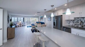 A modern kitchen with white cabinets, stainless steel appliances, and a central island with bar stools. - Free Kayaks Overlooking Pickleball Courts (Key Largo)