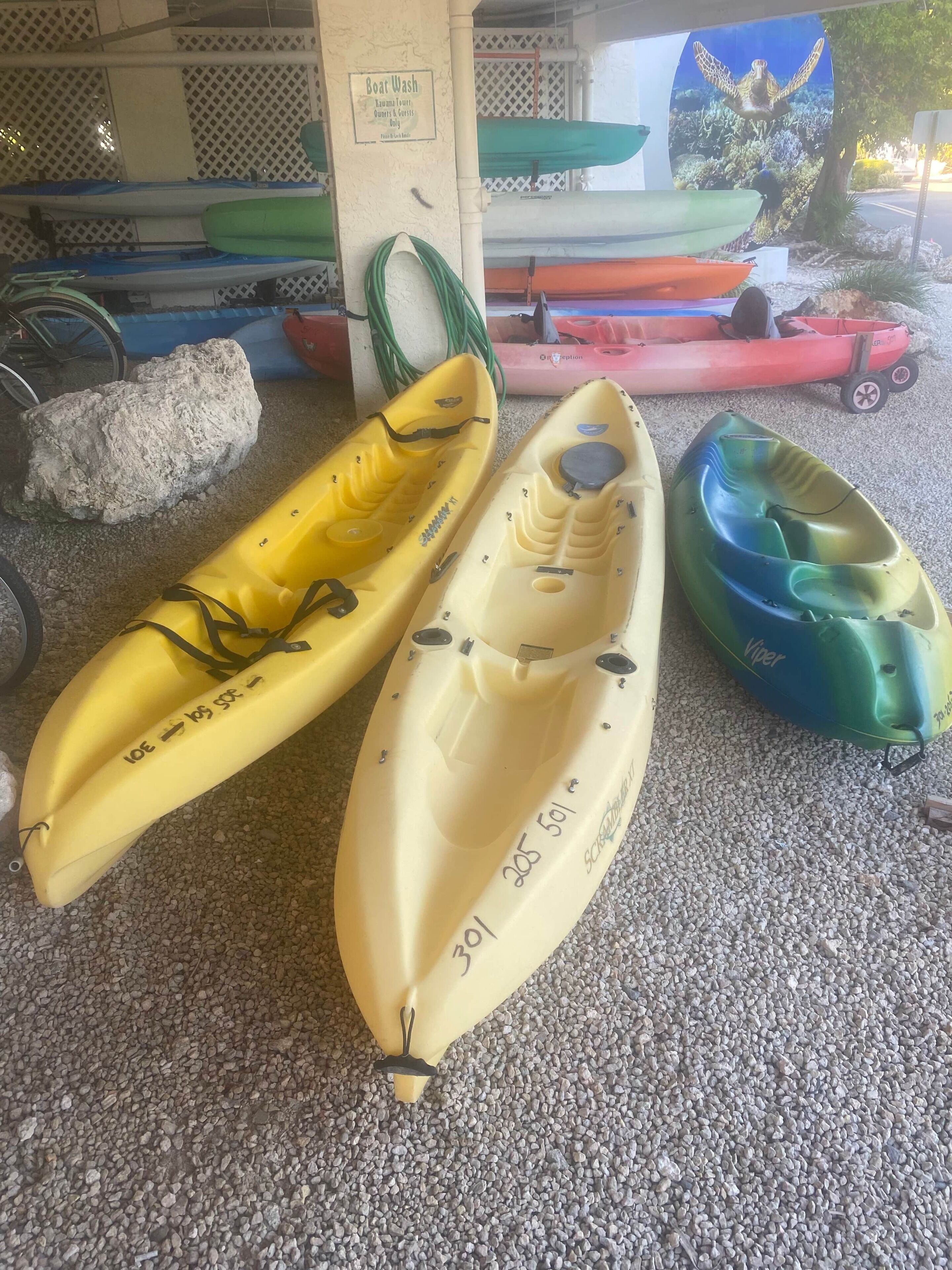 Three kayaks, a rock, and a sign for a boat wash.