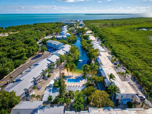 Ein Luftbild eines Resorts mit einem zentralen Schwimmbecken, mehreren Gebäuden und freiem Blick auf den Ozean.