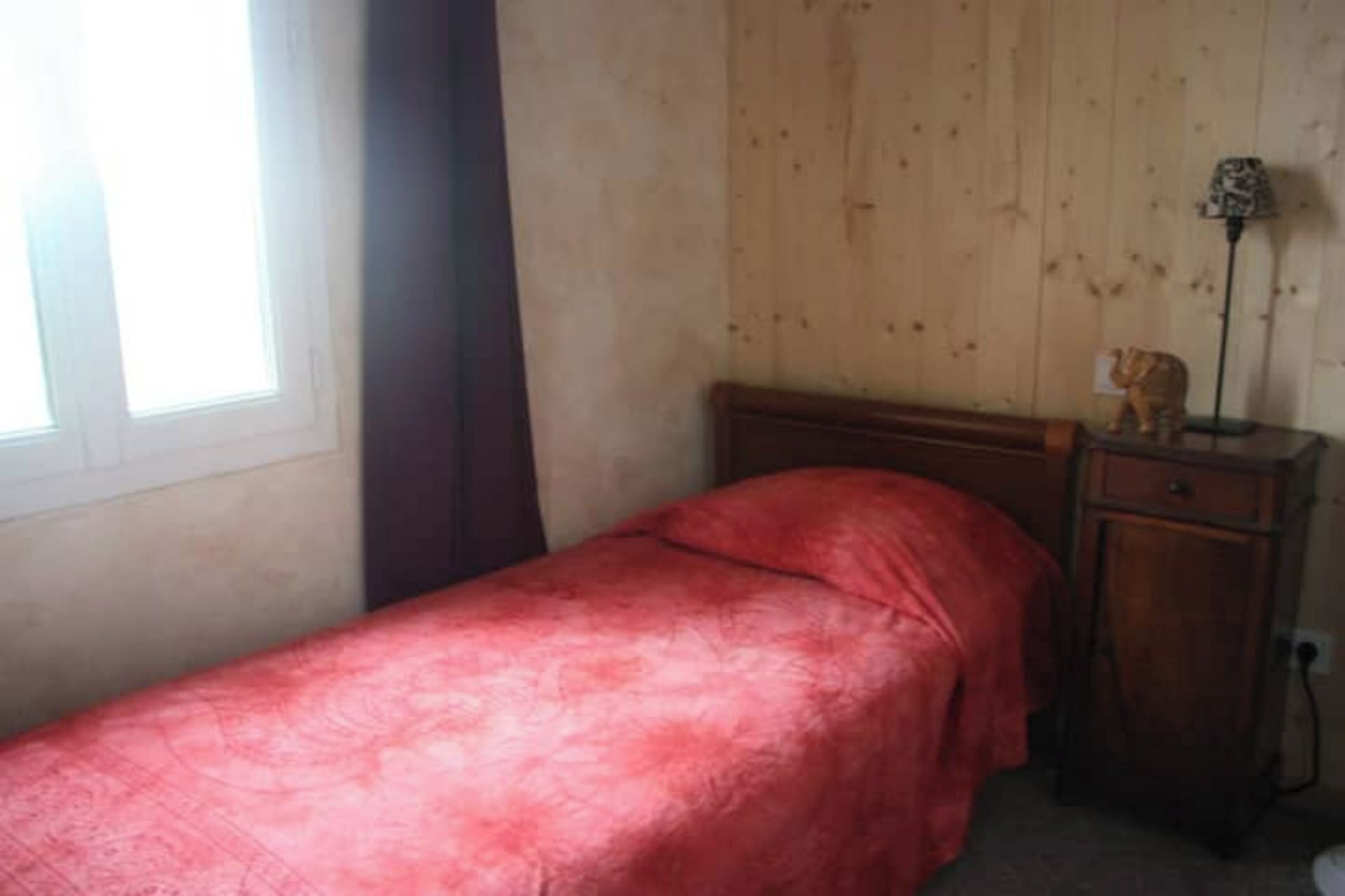 A small bedroom with a single bed, a wooden nightstand, and a lamp.