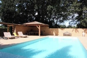 Piscina azul cristalina con sillas de descanso y un área de estar cubierta.