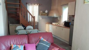 Un salon avec un canapé en cuir rouge, un escalier, un coin cuisine et une table à manger avec des chaises.