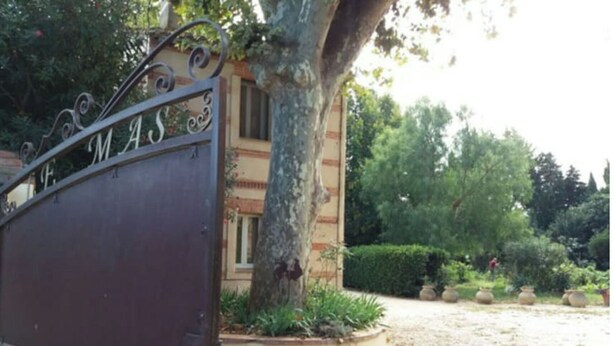 Une entrée fermée par un portail en métal sur lequel on peut lire l’inscription « MAS ».
