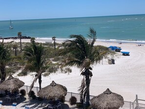 Vista de una playa con sombrillas de techo de paja, palmeras y arena.