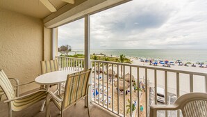 A balcony with a table and chairs, overlooking a beach with umbrellas and people.