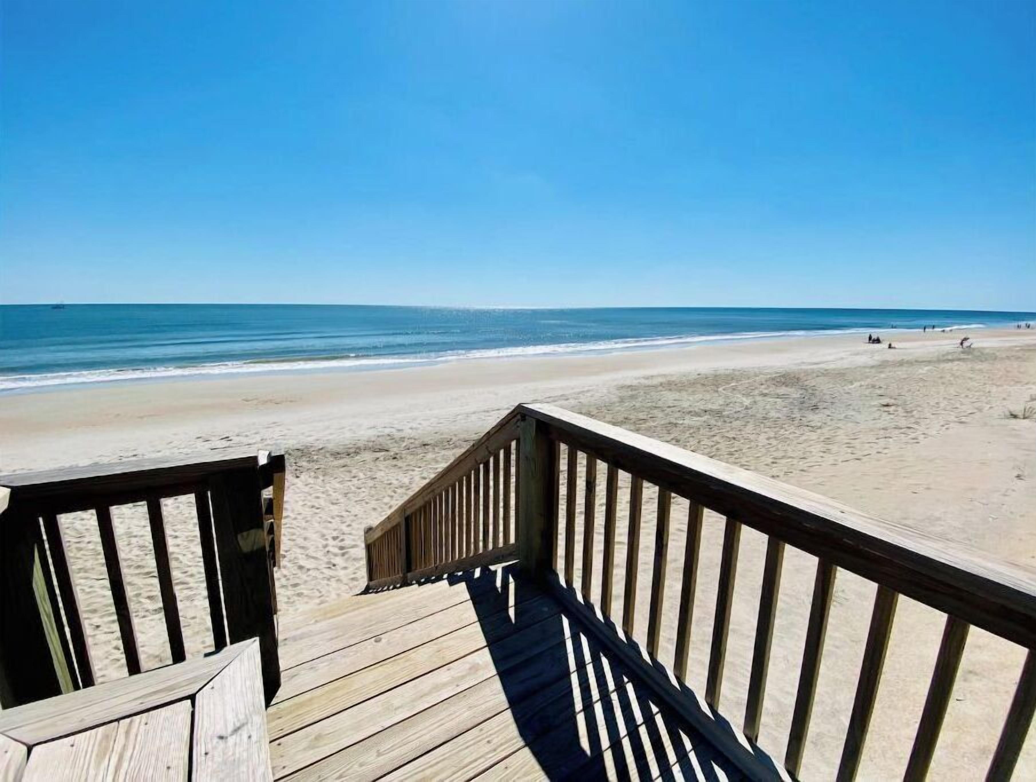 A wooden deck leading to a beach with a clear view of the ocean.