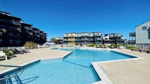 A swimming pool area with a 2ft depth marker, surrounded by modern buildings and lounge chairs.