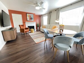 Uma sala de estar moderna com lareira, ventilador de teto e área de jantar com mesa redonda e cadeiras.
