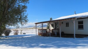 A single-story house with a covered porch, a snow-covered landscape, and mountains in the background. - Chesterfield-Lava Hot Springs - Farm Cottage (Bancroft)