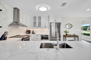 Una cocina moderna con encimeras de mármol blanco, electrodomésticos de acero inoxidable y una isla central con pileta.
