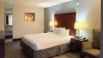 A hotel room with a large bed, two bedside lamps, a chair, a wooden headboard, and a painting on the wall.