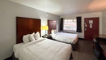 A hotel room with two beds, a desk, a lamp, and a window with curtains.