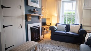 A cozy living room with a fireplace, a sofa, a television, and a window with curtains. - Brakestone Cottage in the heart of Port Isaac (Port Isaac)