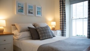 A neatly made bed with pillows, a bedside lamp, and a window with curtains. - Brakestone Cottage in the heart of Port Isaac (Port Isaac)