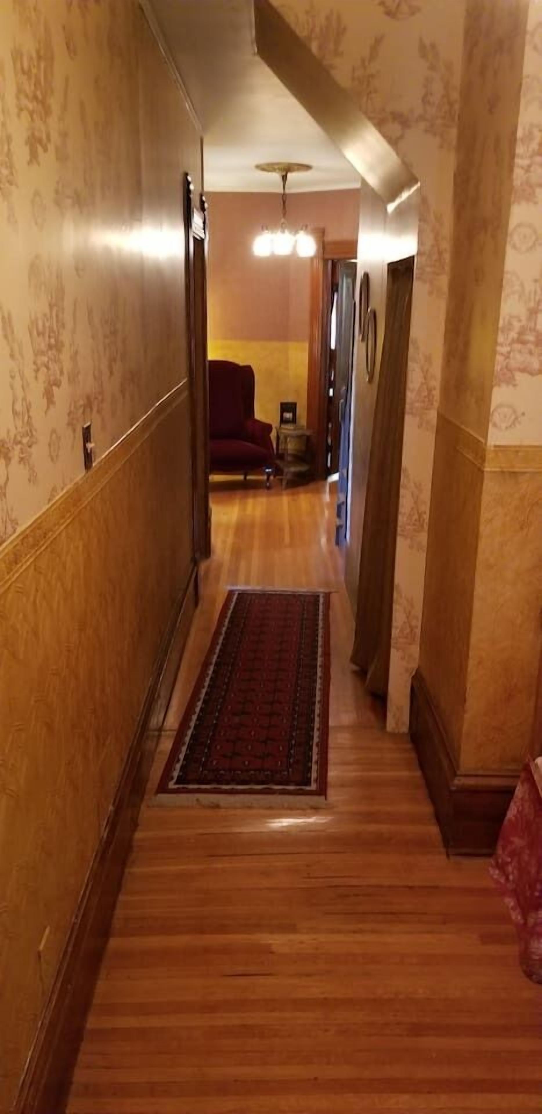 A narrow hallway with wooden flooring and patterned wallpaper.
