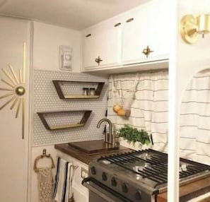 A kitchen with a stove, sink, and decorative wall shelves. - Pleasant Hills Farm Stargazer Farmstay (Darnestown)