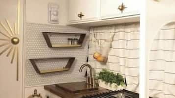 A kitchen with a stove, shelves, and a decorative wall piece.