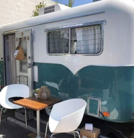 Una caravana antigua con comedor que incluye dos sillas blancas y una mesa de madera.
