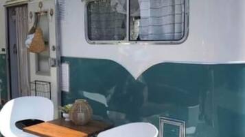 Una caravana antigua con comedor que incluye dos sillas blancas y una mesa de madera.