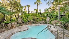 A swimming pool with a stone border, surrounded by tropical vegetation and rocks.