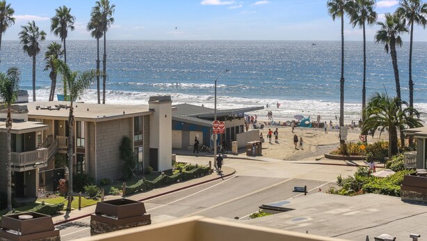 Un hotel frente a la playa con vista al océano, palmeras y un paseo peatonal.