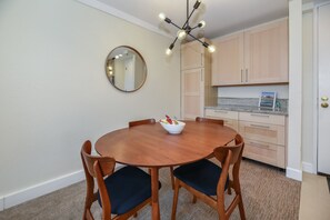 Un comedor con una mesa redonda de madera, cuatro sillas, un cuenco de fruta, un espejo redondo y una lámpara moderna.