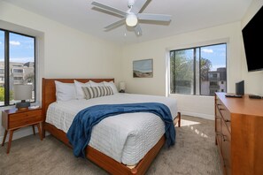 Un dormitorio con cama, ventilador de techo, un cuadro, televisor y cómoda.