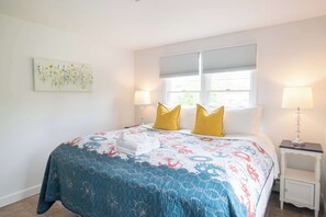 Un dormitorio con una cama, dos lámparas de noche, una mesita de noche y un ventanal con persianas.