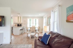 Ein modernes Wohnzimmer mit einer braunen Ledersofa, einem Essbereich mit Tisch und Stühlen sowie einer Küche mit weißen Schränken.