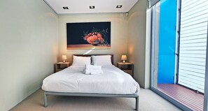 Un letto rifatto con lenzuola bianche, due comodini con lampade, un quadro sopra il letto e un'ampia finestra con vista.